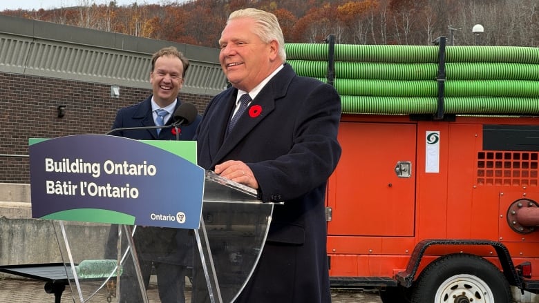 A man at a podium with another man in the background.