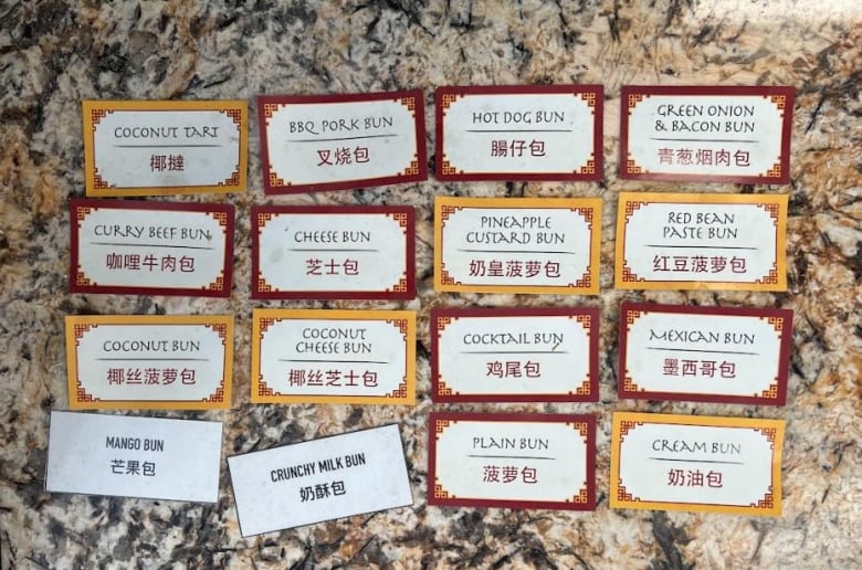 Sixteen cards with menu items written in English and Chinese are seen lined up on a kitchen table.