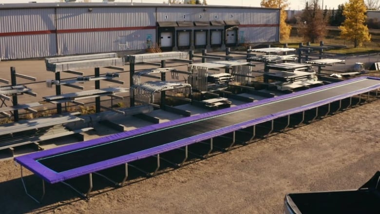 In a field outside is a 100 foot stretch of a trampoline that has a vinyl purple lining on the outside. 