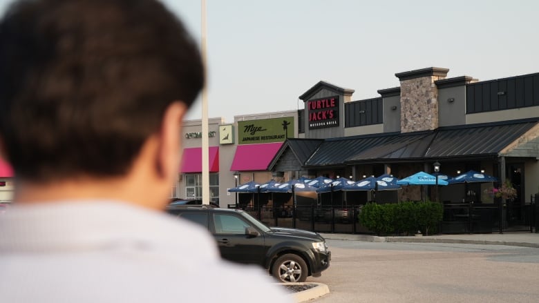 A person, out of focus, faces away from the camera while looking at the front entrance for Turtle Jacks in Oakville, Ont.