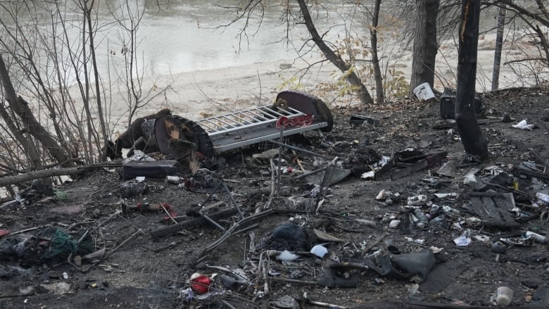 Blackened ground and charred debris can be seen along a river bank.