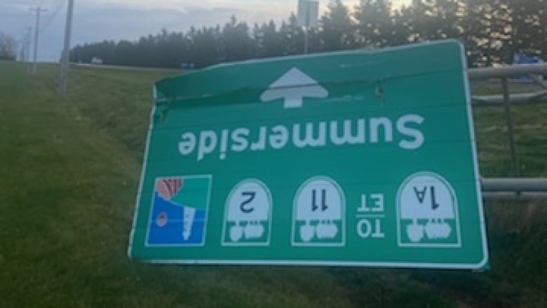 A green highway sign reading 'Summerside' is shown damaged in a roadside ditch. 