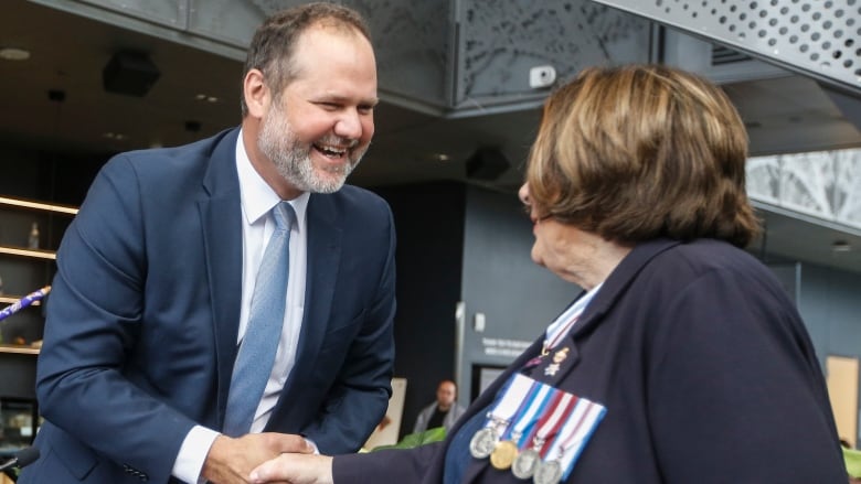 a man shaking hands with a woman wearing a suit with medals.