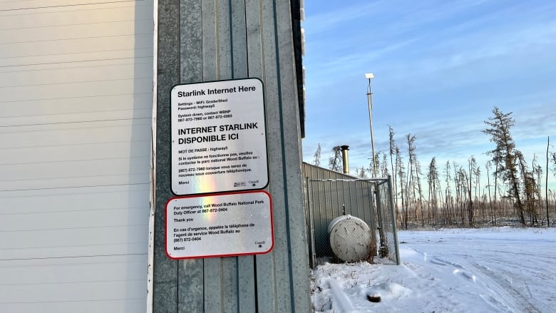 A Starlink dish sits on a long pole along side a board with login info posted to a shed.