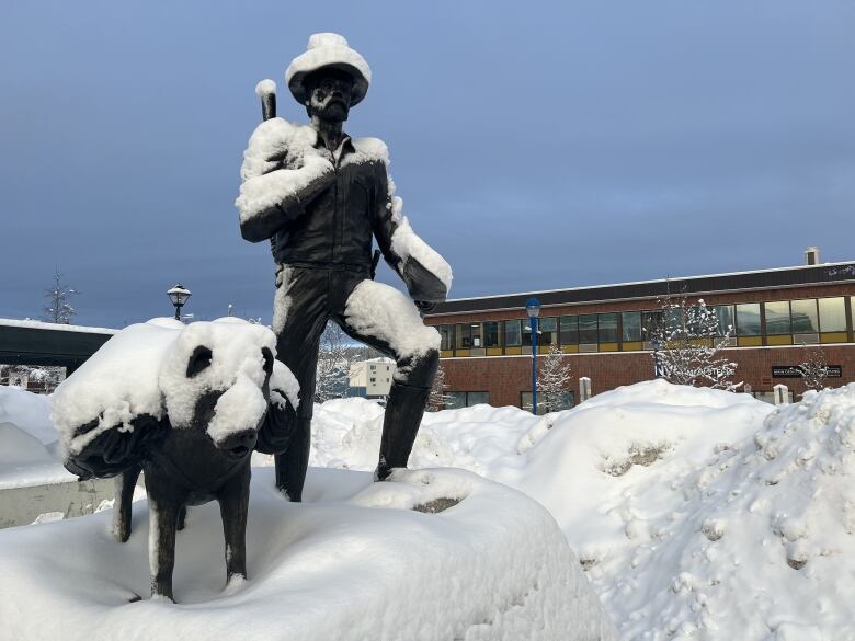 A snow-covered statue of a man and a dog, on a city street.