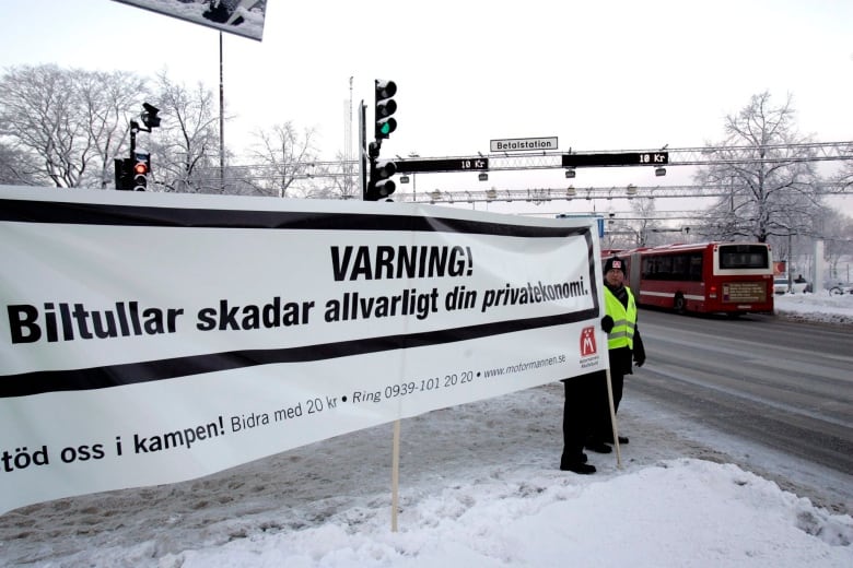 Protesters stand in the snow holding a big white banner that reads in Swedish: 'Warning! Congestion charges seriously hurt your private economy.'