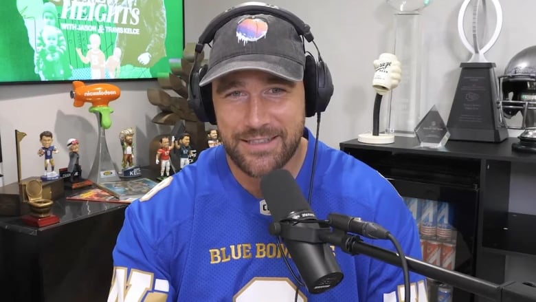 A man wearing headphones and a football jersey speaks into a microphone.