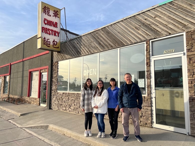 A family of four stand outside a store front with a large yellow and red sign that says 'China Pastry.' Two younger women with darker hair stand on the right, while an older couple stand on the left.