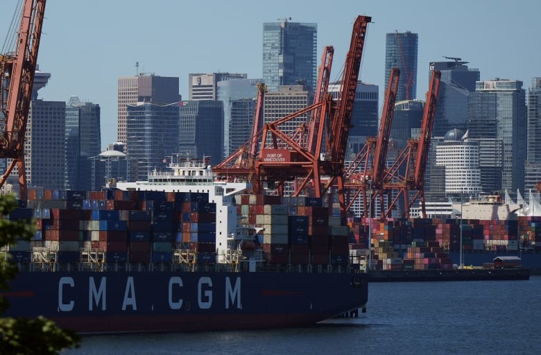 A large ship-unloading crane or gantry sits on the docks facing the water with the City of Vancouver skyline behind it.