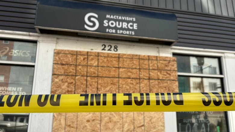 A storefront with boards on it and a piece of caution tape blocking the entrance.