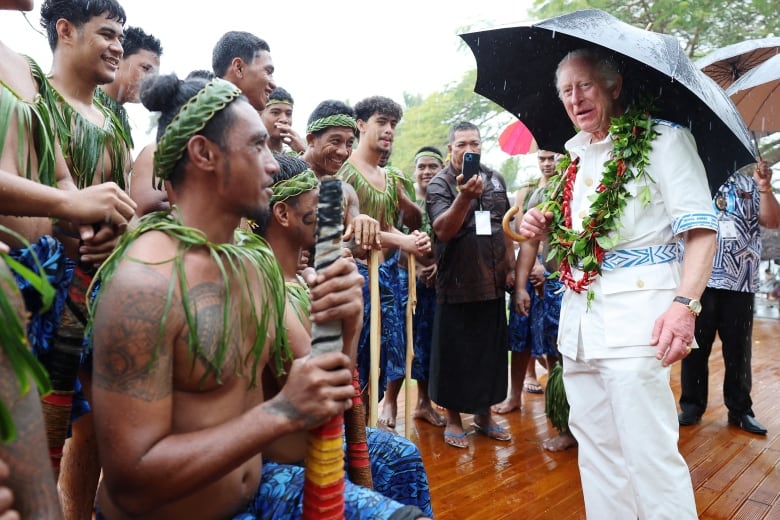 A person holding an umbrella talks to other people who are lined up.