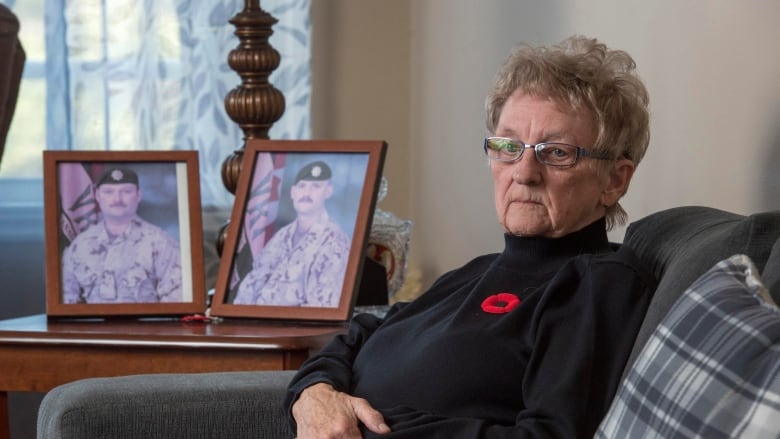 An older woman sits next to two photos of men in military uniforms.