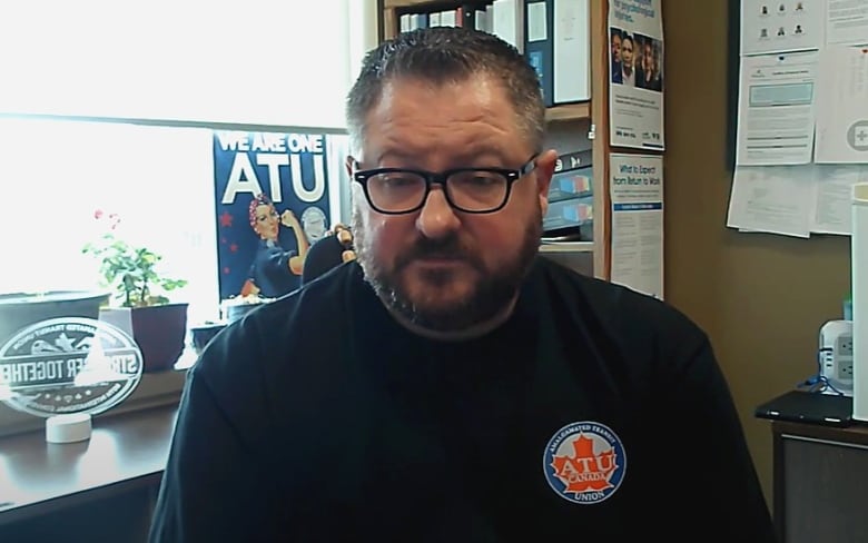 A man with short hair and eyeglasses sits at a desk