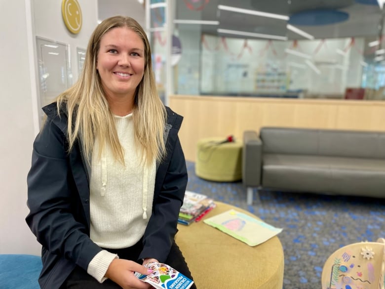 A woman with long blonde hair sits on an armchair in a public library.