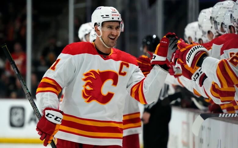 A man wearing hockey equipment and the white and red Calgary Flames team kit high-fives teammates.