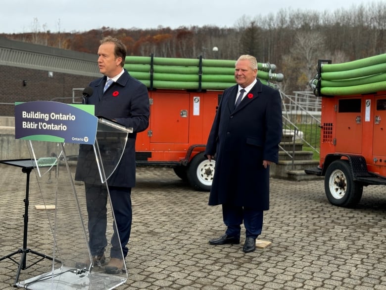 A man stands at a podium with another man behind him 