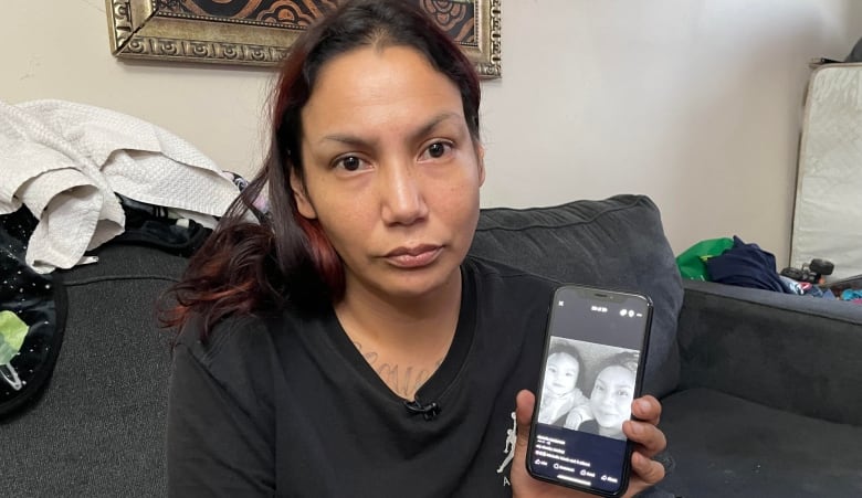 A woman holding up a phone with a black-and-white picture of her and a baby.