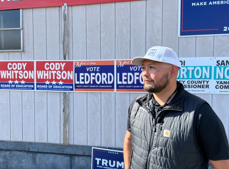 A person is pictured standing in front of a building adorned with political signs.