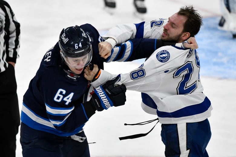 Two hockey players holding each other's jerseys, one with his glove and helmets off.