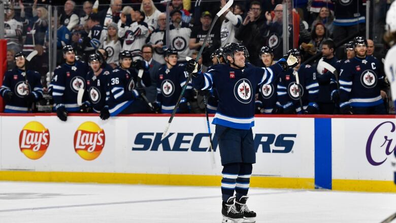 A hockey player stands alone with his arms stretched out on the ice.