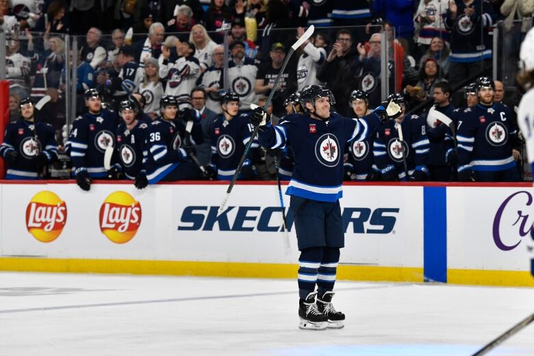 A hockey player stands alone with his arms stretched out on the ice.