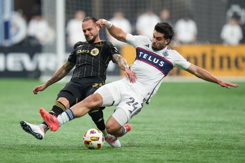 Two players, one in black and another in white try to take control of the ball on the soccer field. 