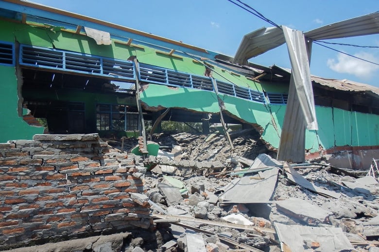 Concrete debris is shown beside a heavily damaged building with a green exterior.