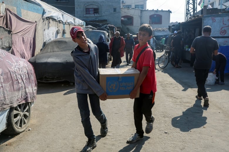 Two boys carrying a box as they walk through a street.