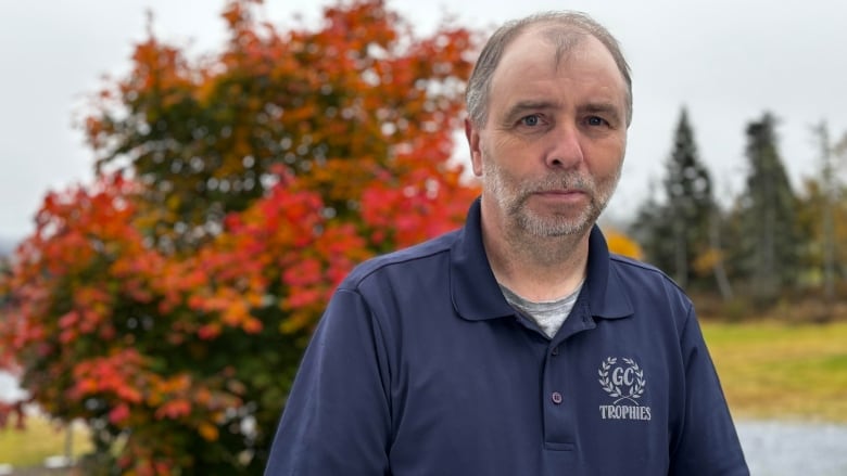 A man in a blue polo shirt looks at the camera. There are autumn leaves behind him.