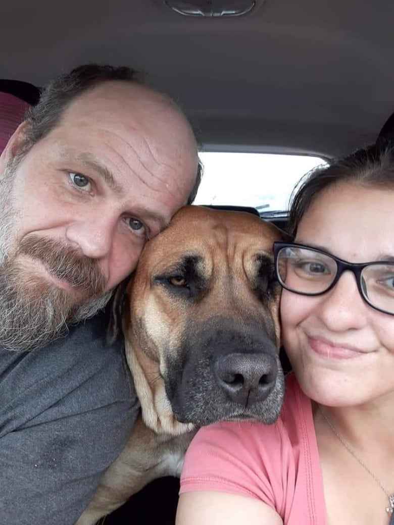 A man and a woman take a selfie with a dog in between their faces.