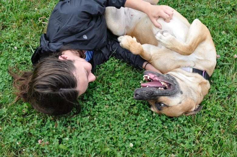 A woman and a dog play while laying down on the grass.