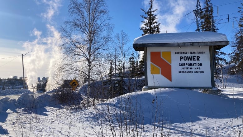 A sign in the snow against a clear blue sky with fumes rising up behind it. 