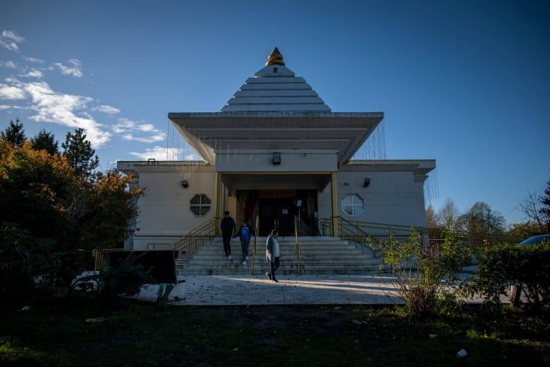 An Indian temple is pictured on a sunny day, with people walking out.