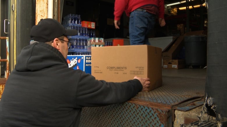 A man lifts a cardboard box off the ramp of a warehouse.