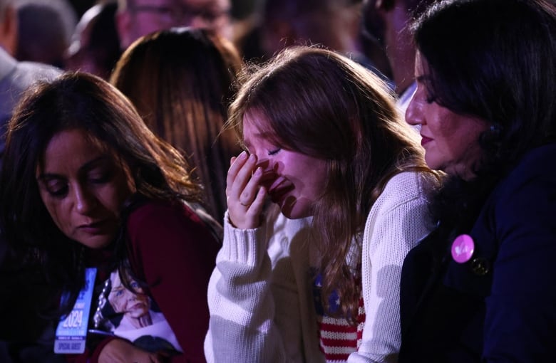 Three young women, with one very emotional and cupping a hand to her face, during election night rally for Kamala Harris.