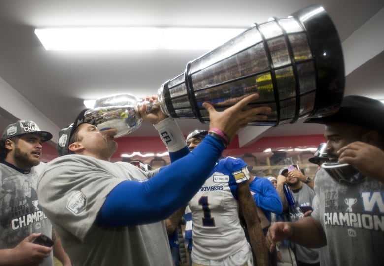 A football player drinks from a big silver trophy