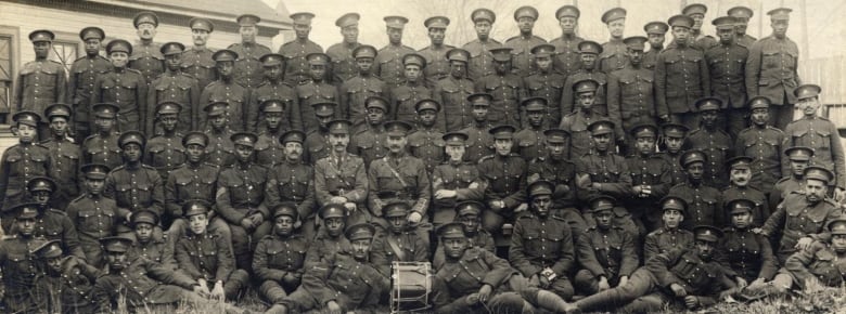 An archive photo shows dozens of Black men in military uniforms, posing for a group photo.