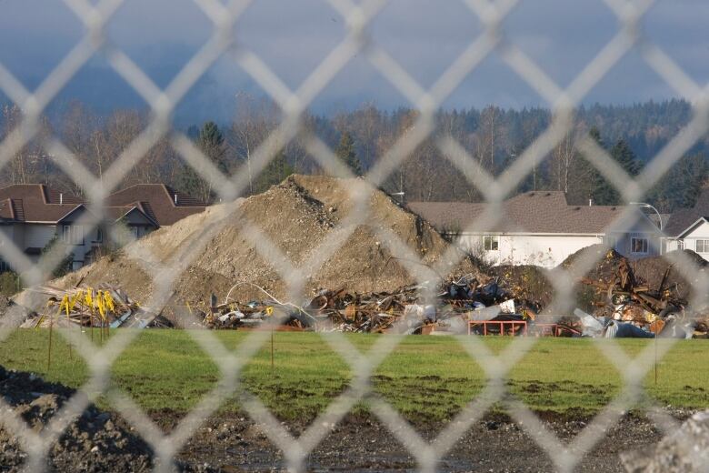 Mounds of dirt and refuse sit behind a chainlink fence.