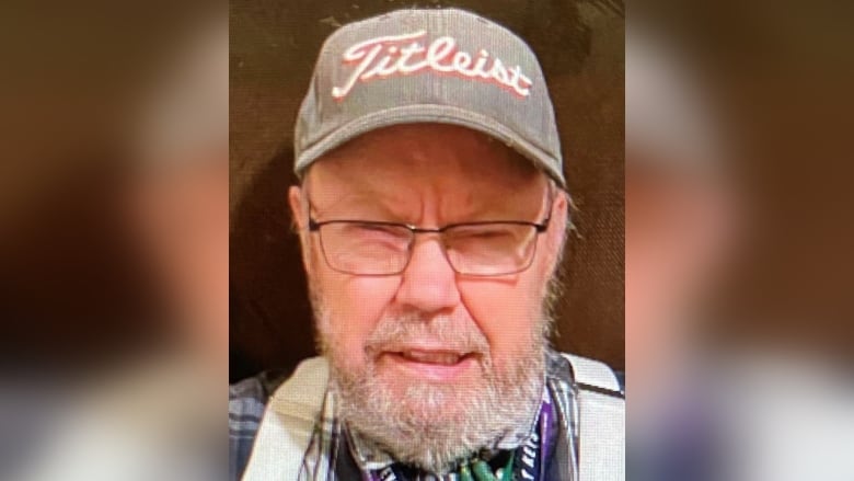 An older man wearing glasses and a cap faces the camera.