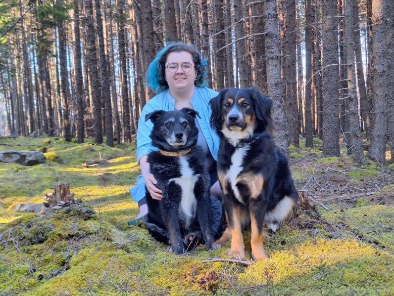 A woman crouches in a forest with two dogs