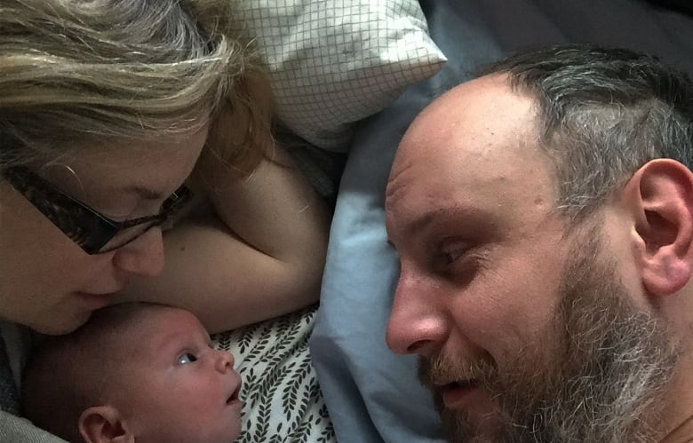 A close up of a man and a baby, with a woman with blonde hair.