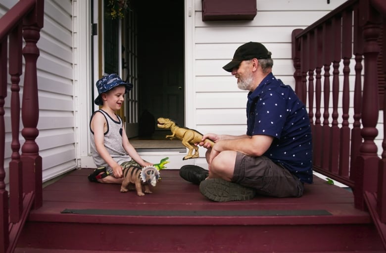 Man and young boy sitting on porch playing with plastic dinosaurs.