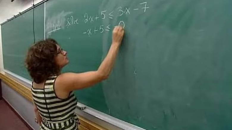 A woman writes math equations on a chalkboard.