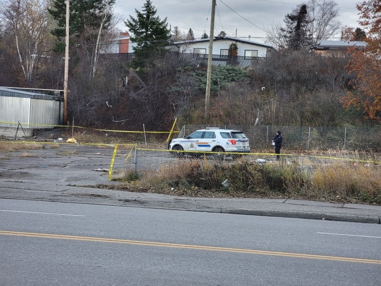 An officer and a police car in an empty lot surrounded by police tape.