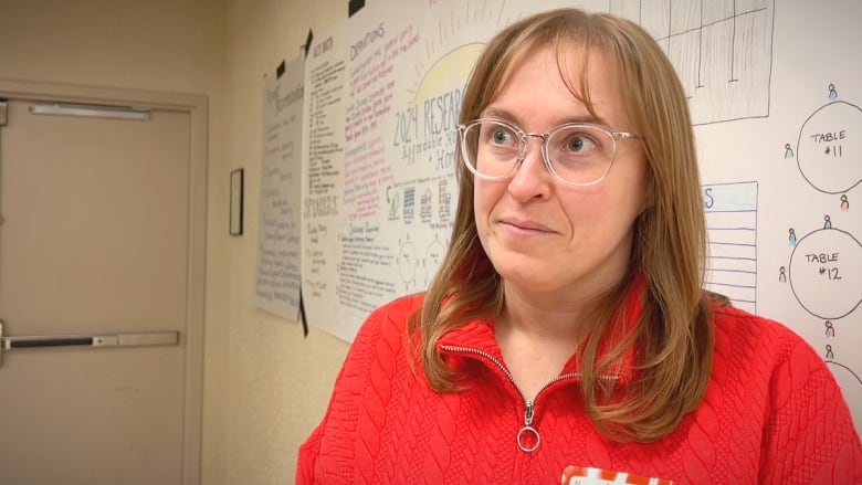 A woman with long brown hair and glasses wearing a red sweater looks away.