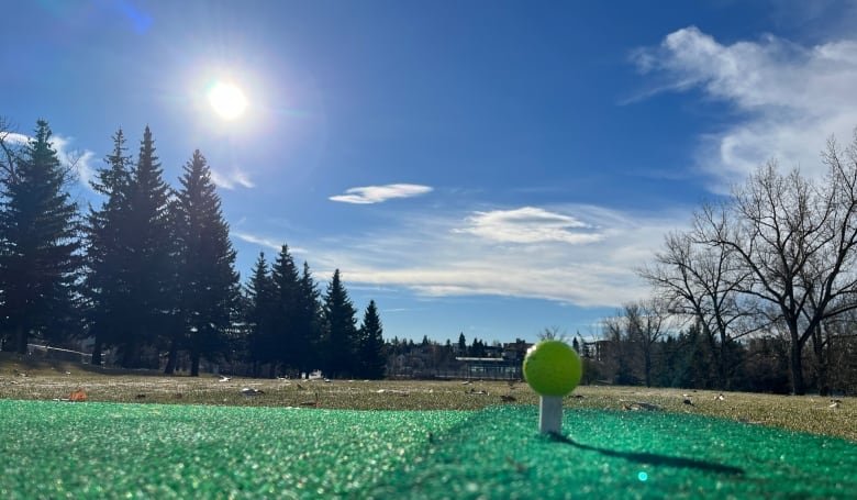 A yellow golf ball pictured on top of a rubber tee on a green golf mat. 