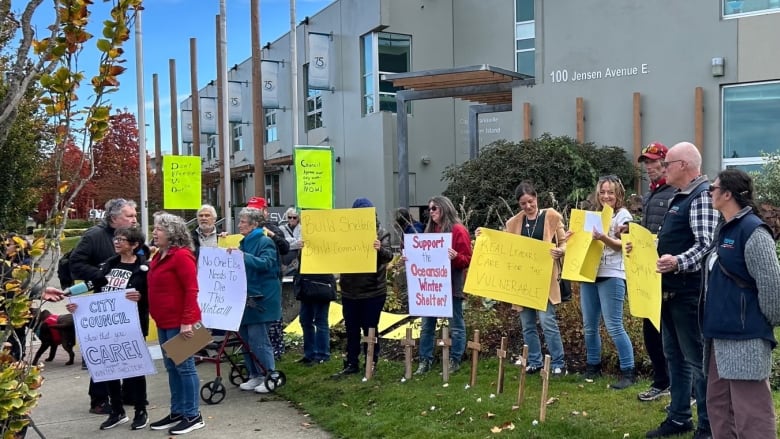 More than a dozen people carry colourful signs in white, yellow and green calling on the city to build a shelter.