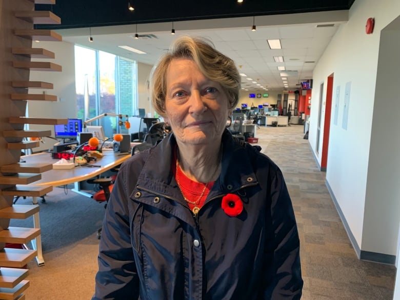 A senior woman wearing a dark jacked an a poppy looks straight at the camera.