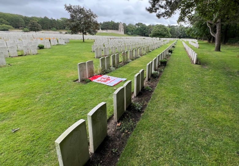 A Canadian flag lies at a cemetery, among lines of soldiers' gravestones 