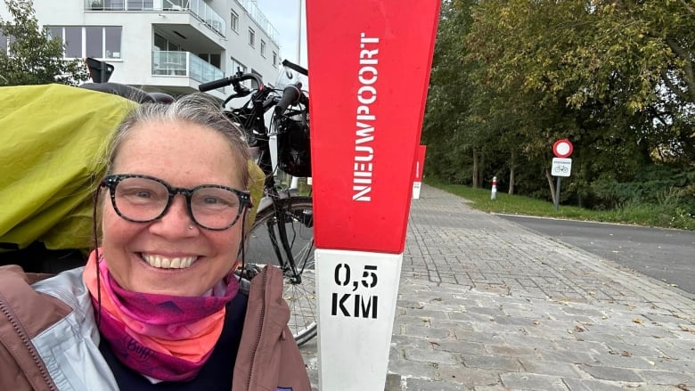 A woman smiles at the camera with a sign behind her 